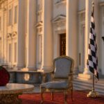 Ein leerer prunkvoller Stuhl vor dem Haupteingang von Schloss Bellevue, flankiert von einem roten Rosenbouquet und einer