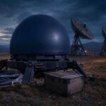 Ein massiver, abgeschirmter Satellitenkommunikations-Terminal mit dunkelblauer Kuppel auf einem abgelegenen Feld, neben ihm