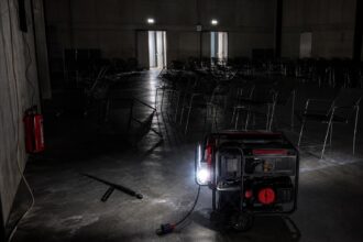 Ein fast dunkler Saal mit einem einsatzbereiten Notstromgenerator, umgeben von leeren Metallstühlen und einem umgestürzten