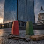 Ein Hochhaus spiegelt den Himmel, dahinter eine Kuppel. Vor dem Gebäude liegen ein Schlüssel, rote und grüne Betonblöcke und